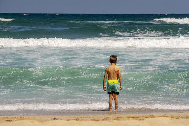 Boy standing on beach looking at waves